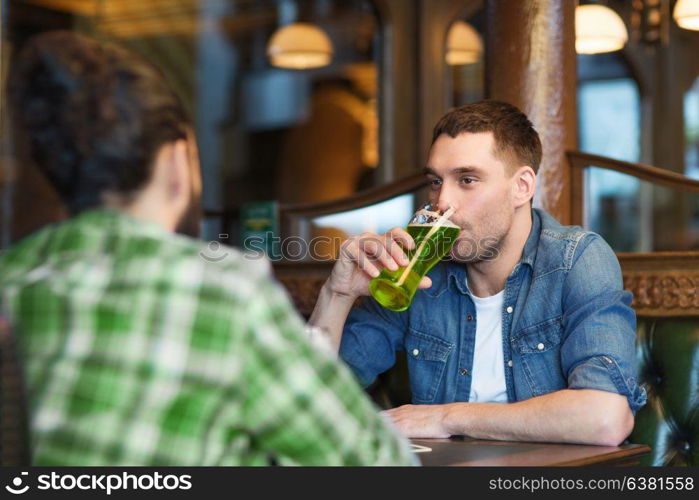 people, leisure and st patricks day concept - happy male friends drinking green beer at bar or pub. male friends drinking green beer at bar or pub