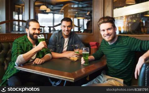 people, leisure and st patricks day concept - happy male friends drinking green beer at bar or pub. male friends drinking green beer at bar or pub