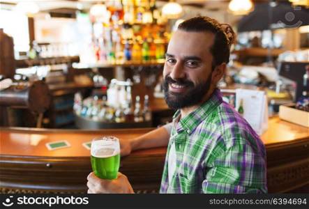 people, leisure and st patricks day concept - happy man drinking green beer at bar or pub. man drinking green beer at bar or pub