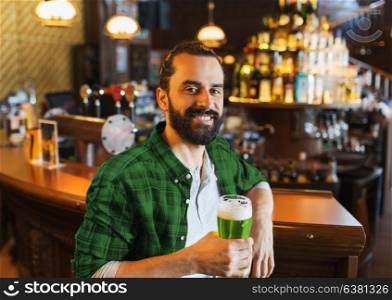 people, leisure and st patricks day concept - happy smiling man drinking green beer at bar or pub. happy man drinking green beer at bar or pub