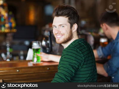 people, leisure and st patricks day concept - happy smiling young man drinking green beer at bar or pub. happy man drinking green beer at bar or pub