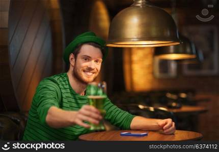 people, leisure and st patricks day concept - happy young man drinking green beer at bar or pub. smiling man drinking green beer at bar or pub