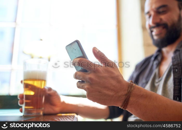 people, leisure and technology concept - close up of man with smartphone drinking beer and reading message at bar or pub