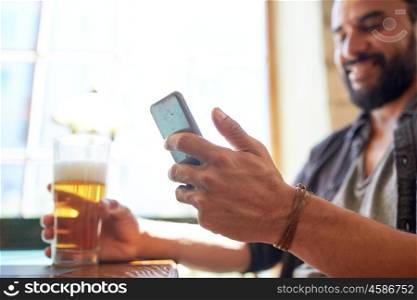 people, leisure and technology concept - close up of man with smartphone drinking beer and reading message at bar or pub