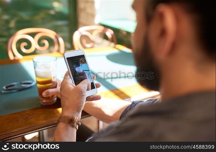 people, leisure and technology concept - close up of man with smartphone photographing beer at bar or pub