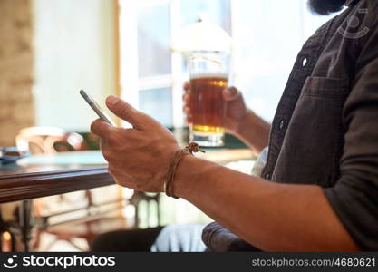 people, leisure and technology concept - close up of man with smartphone drinking beer and reading message at bar or pub