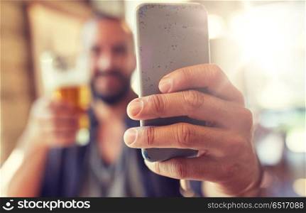 people, leisure and technology concept - close up of man with smartphone drinking beer and taking selfie at bar or pub. close up of man with smartphone and beer at pub. close up of man with smartphone and beer at pub