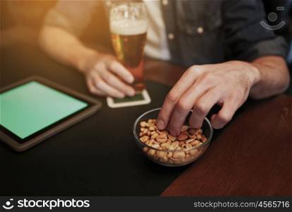 people, leisure and technology concept - close up of man with tablet pc computer drinking beer and eating peanuts at bar or pub