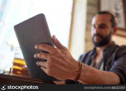 people, leisure and technology concept - close up of man with tablet pc computer drinking beer at bar or pub
