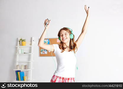 people, leisure and technology concept - happy woman or teenage girl in headphones listening to music from smartphone and dancing on bed at home