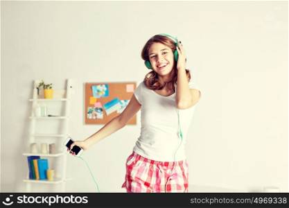 people, leisure and technology concept - happy woman or teenage girl in headphones listening to music from smartphone and dancing on bed at home. happy woman in headphones ihaving fun at home