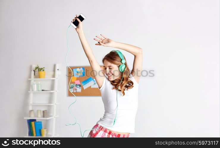 people, leisure and technology concept - happy woman or teenage girl in headphones listening to music from smartphone and dancing on bed at home