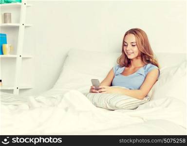 people, leisure and technology concept - happy woman or teenage girl with smartphone in bed at home. happy woman or girl with smartphone in bed at home