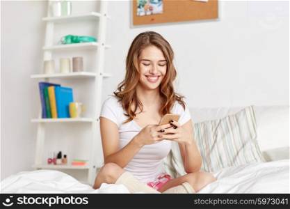 people, leisure and technology concept - happy woman or teenage girl with smartphone in bed at home
