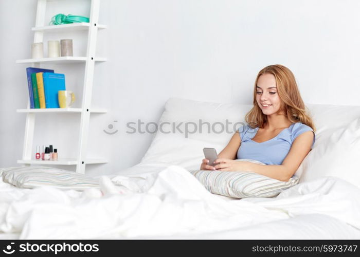 people, leisure and technology concept - happy woman or teenage girl with smartphone in bed at home