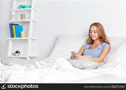 people, leisure and technology concept - happy woman or teenage girl with smartphone in bed at home