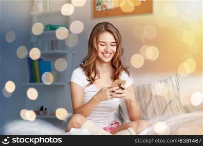 people, leisure and technology concept - happy woman or teenage girl with smartphone in bed at home. happy woman or girl with smartphone in bed at home