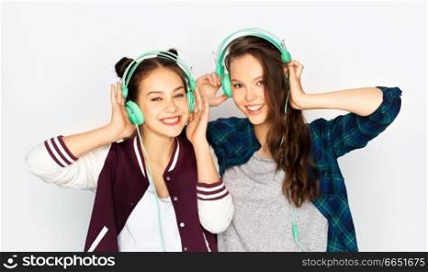 people, leisure and technology concept - smiling teenage girls in earphones listening to music over white background. teenage girls in earphones listening to music
