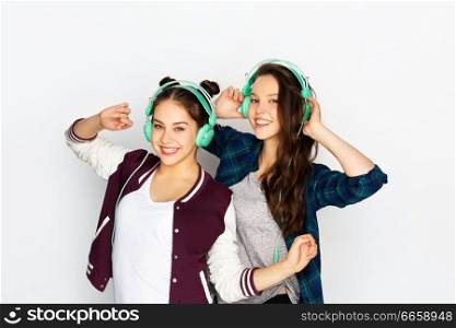 people, leisure and technology concept - smiling teenage girls in earphones listening to music and dancing over white background. teenage girls in earphones listening to music