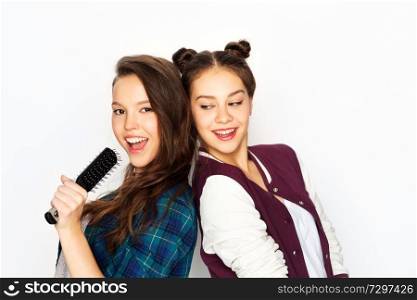 people, leisure and technology concept - smiling teenage girls in earphones listening to music and singing to hairbrush and having fun over white background. teenage girls singing to hairbrush and having fun