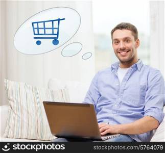 people, leisure and technology concept - smiling young man with laptop computer and trolley icon shopping online at home