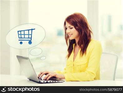 people, leisure and technology concept - smiling young woman with laptop computer and trolley icon shopping online at home