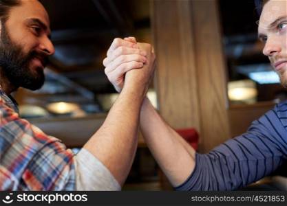 people, leisure, challenge, competition and rivalry concept - close up of male friends arm wrestling at bar or pub