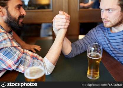 people, leisure, challenge, competition and rivalry concept - happy male friends arm wrestling and drinking draft beer at bar or pub