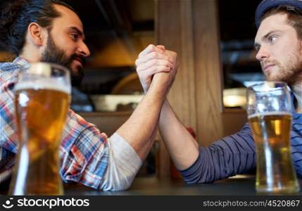people, leisure, challenge, competition and rivalry concept - male friends arm wrestling and drinking draft beer at bar or pub