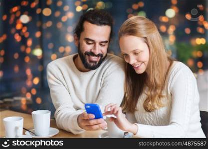 people, leisure, communication and dating concept - happy couple with smartphone drinking tea or coffee at cafe over holidays lights background