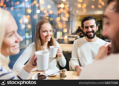 people, leisure, communication and friendship concept - happy friends meeting and drinking tea at cafe over holidays lights