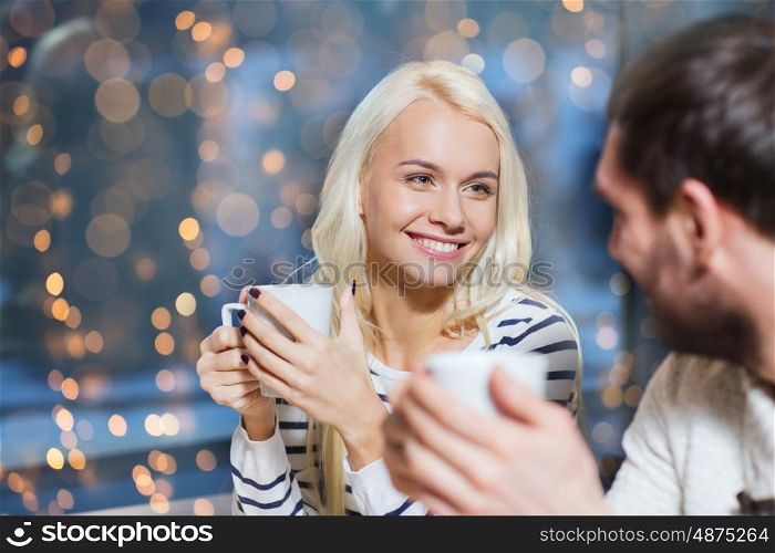 people, leisure, communication, eating and drinking concept - happy couple meeting and drinking tea or coffee at cafe over holidays lights background