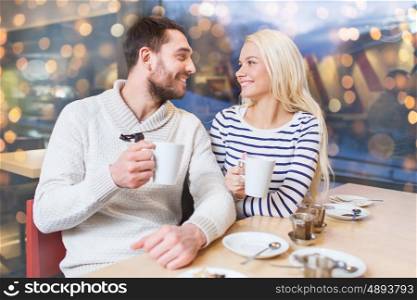 people, leisure, communication, eating and drinking concept - happy couple meeting and drinking tea at cafe over holidays lights background