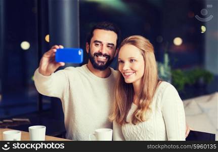 people, leisure, communication, eating and drinking concept - happy couple with smartphone taking selfie at cafe