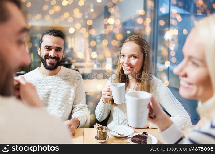 people, leisure, communication, eating and drinking concept - happy friends meeting and drinking tea at cafe over holidays lights background