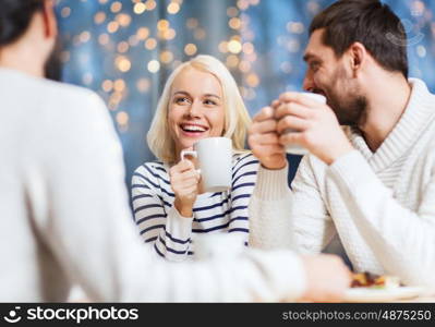 people, leisure, communication, eating and drinking concept - happy friends meeting and drinking tea or coffee at cafe over holidays lights background