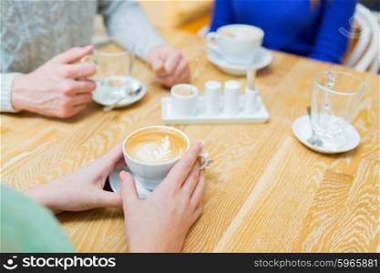 people, leisure, drink and latte art concept - close up of hands with coffee cup at cafe