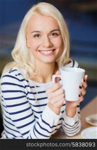 people, leisure, eating and drinking concept - happy young woman drinking tea or coffee at cafe or home