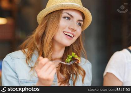 people, leisure, food and communication concept - group of happy smiling young woman with fork eating salad and meeting friends at bar or pub