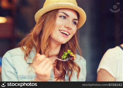people, leisure, food and communication concept - group of happy smiling young woman with fork eating salad and meeting friends at bar or pub