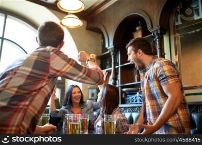people, leisure, friendship and celebration concept - happy friends with beer celebrating victory at bar or pub