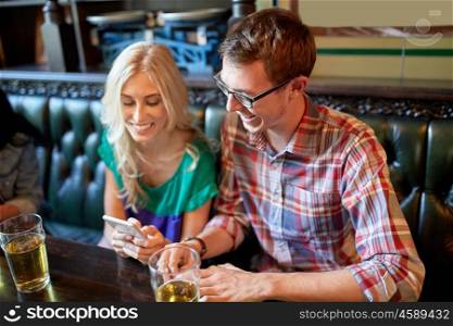 people, leisure, friendship and communication concept - friends with smartphones drinking beer and texting at bar or pub