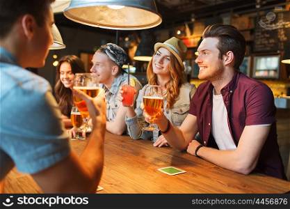 people, leisure, friendship and communication concept - group of happy smiling friends drinking beer and cocktails talking at bar or pub