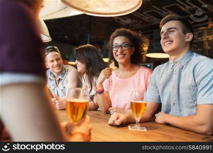 people, leisure, friendship and communication concept - group of happy smiling friends drinking beer and talking at bar or pub