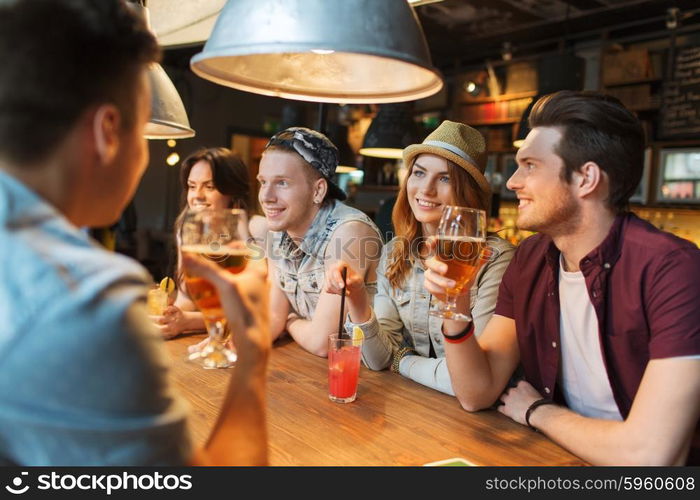 people, leisure, friendship and communication concept - group of happy smiling friends drinking beer and cocktails talking at bar or pub