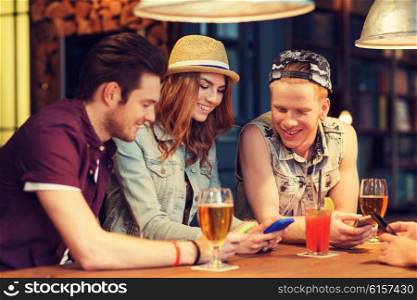 people, leisure, friendship and communication concept - group of happy smiling friends with smartphones and drinks at bar or pub