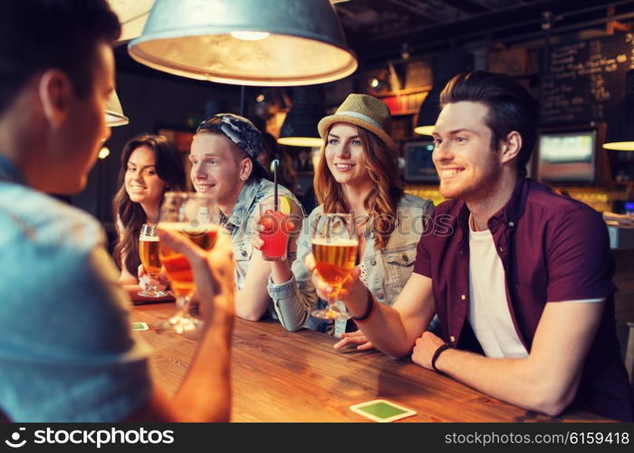 people, leisure, friendship and communication concept - group of happy smiling friends drinking beer and cocktails talking at bar or pub