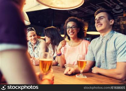 people, leisure, friendship and communication concept - group of happy smiling friends drinking beer and talking at bar or pub