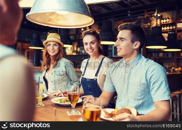 people, leisure, friendship and communication concept - group of happy smiling friends eating, drinking and talking at bar or pub