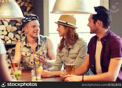 people, leisure, friendship and communication concept - group of happy smiling friends drinking beer and cocktails at bar or pub